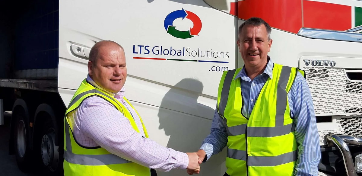 Two men shaking hands in front of an LTS truck